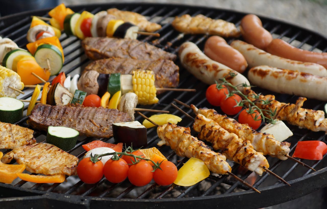 A grill cooking burgers, vegetables, hot dogs, and other healthy summer foods.