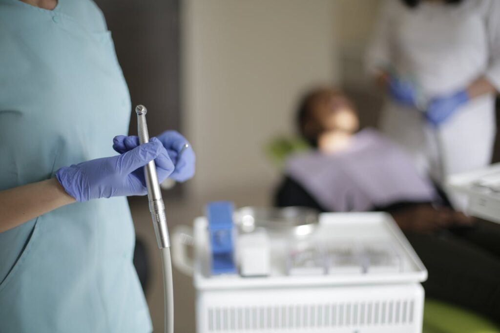 Dentist holding dental toothbrush with other tools and patient blurred in background